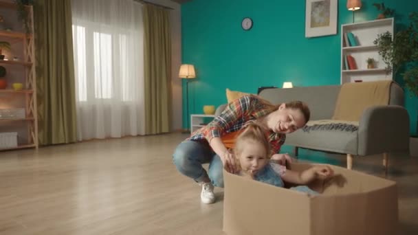 妈妈和她的小女儿玩得很开心 快乐的年轻妈妈蹲在纸盒旁边 她的小女儿坐在纸盒里吃棒棒糖 家庭关系概念 — 图库视频影像