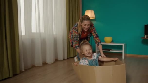 妈妈和小女儿玩得很开心妈妈正在把一个纸板箱推倒在地板上 小女孩就坐在纸板箱里 关门了 慢动作 — 图库视频影像