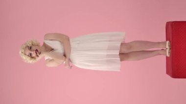 Şehvetle gülümseyen ve parmaklarıyla dudaklarına dokunan güzel bir kadının portresi. Marilyn Monroe suretinde bir kadın pembe bir stüdyoda kırmızı bir kaidede dikiliyor.