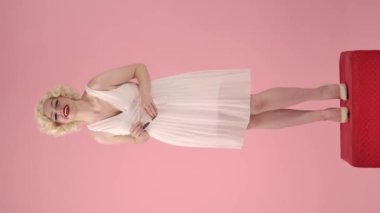 Kadın elinde güneş gözlüğü tutuyordu ve eliyle ağzını kapatırken gülüyordu. Marilyn Monroe 'nun görüntüsündeki kadın pembe arka plandaki kırmızı bir kaidede dikiliyor.