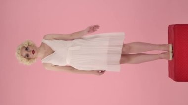 Şaşırmış kadın elini yana doğru tutar, onaylayarak başını sallar, tavsiye eder. Marilyn Monroe gibi bir kadın pembe arka planda kırmızı kaidede dikiliyor. Dikey video