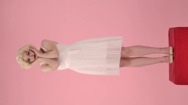 Stüdyoda pembe arka planda kırmızı kaidedeki neşeli genç kadının tam boy portresi. Marilyn Monroe 'nun suretinde bir kadın yüzünü avuçlarının içinde tutuyor, saçını düzeltiyor. Dikey