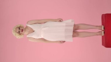 Kadın hoş olmayan bir kokudan tiksiniyor, ya da tadıyor, ağzını eliyle kapatıyor, el sallıyor. Marilyn Monroe 'nun görünümünde bir kadın pembe bir stüdyoda kırmızı bir kaidede dikiliyor.