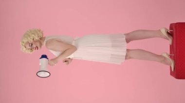 Marilyn Monroe karakterindeki kadının megafona konuşmasının yan görüntüsü. Kırmızı kaidede duran muhteşem kadın stüdyoda pembe arka planda. Dikey video. Satış, Kara Cuma. Anlaşıldı.