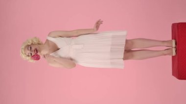 Kadın, renkli bir lolipop gösterdiğini söylüyor. Bir kadın çubuğun üzerindeki şekeri yalıyor, gözünü lolipopla kaplıyor ve onu öpüyor. Marilyn Monroe 'nun görüntüsü, kaidede dimdik duran kadın.