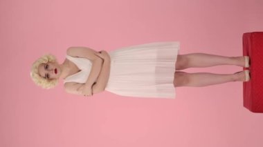 Kollarını göğsüne bağlamış bir kadın, lolipop teklif edilene kadar üzülür. Kadın, şekeri kabul edip yaladığı için mutlu. Marilyn Monroe 'nun suretindeki kadın kaidede dimdik ayakta duruyor.