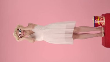 Kadın 3D gözlük takıyor, patlamış mısır alıyor ve film izliyor. Patlamış mısır yiyen bir kadın, filmin konusunu merak ediyor. Marilyn Monroe 'nun fotoğrafındaki kadın stüdyoda kaidede dimdik duruyordu.