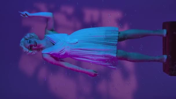 石鹸の泡に囲まれて踊る女性は 空気のキスを送ります ピンクとネオンライトのマリリンモンローのイメージの女性は ハイライト付きのスタジオのペダルに完全な長さを立っています バーティカルビデオ — ストック動画