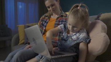 Annem kızına dizüstü bilgisayarda çalışmayı öğretiyor. Cihazın çalışma prensibini anlatıyor ve ona gösteriyor. Anne ve kızı oturma odasındaki kanepede oturmuş internette oyun oynuyorlar.
