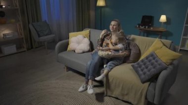 Mutlu anne oturma odasındaki kanepede oturmuş küçük kızına sarılıp televizyon izliyor ve büyük bir tabaktan patlamış mısır yiyor. Anne ve kızı gülüyor, komik bir film, çizgi film veya video HDR izliyor.