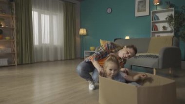 Anne küçük kızıyla eğleniyor. Neşeli genç anne, küçük kızının oturup lolipop yediği bir karton kutunun yanına çömeliyor. Aile İlişkileri Konsepti HDR BT2020 HLG Malzemeleri