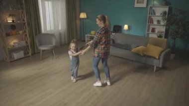 Küçük kız ve sevgili anne oturma odasında el ele tutuşup dans ediyorlar. Aile birlikte eğleniyor, olumlu duyguların tadını çıkarıyor. Aile İlişkileri Konsepti HDR BT2020 HLG Malzemeleri