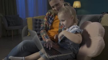 Bir anne küçük kızına bilgisayar uygulamalarıyla nasıl çalışacağını öğretiyor. Anne ve kızı oturma odasında kanepede oturup online oyun oynuyorlar, çocuklar için eğitim uygulamaları öğreniyorlar, daktilo yazıyorlar.