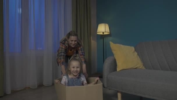 ママと小さな娘が楽しんでいる 母親は床に段ボール箱を押し込んでおり その中に少女が座って近づいている スローモーションHdr Bt2020 Hlg材料 — ストック動画