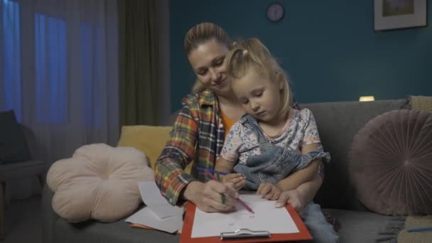Счастливая Мама Помогает Дочери Рисовать Цветными Карандашами Сидя Вечером Диване — стоковое видео