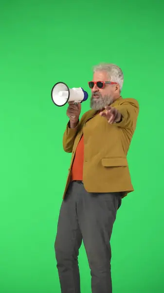Creative modern seniors concept. Portrait of senior stylish hipster on Chroma key green screen background, man talking in megaphone acting cool . Advertising area, workspace mockup. Vertical photo.
