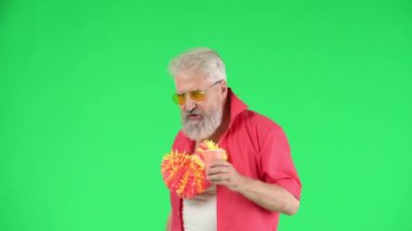 Yaratıcı yaşlılar ve modern yaşam tarzı konsepti. Chroma anahtar yeşil ekranda üst düzey hipster portresi, elinde çiçek çelengi olan adam, partide insanları selamlıyor. Reklam alanı, çalışma alanı modeli.
