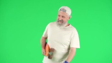 Yaratıcı yaşlılar ve modern yaşam tarzı konsepti. Chroma Key Green ekranında kıdemli hipster portresi, kaykaylı yaşlı adam havalı ve sportif davranan insanları selamlıyor. Reklam alanı, çalışma alanı modeli.