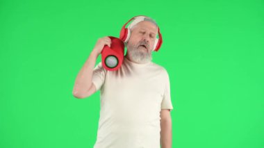 Yaratıcı yaşlılar ve modern yaşam tarzı konsepti. Chroma 'da kıdemli hipsterin portresi yeşil ekranda, kulaklık takan havalı yaşlı adam müzikle çalkalanıyor. Reklam alanı, çalışma alanı modeli.