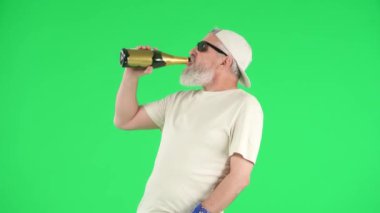 Yaratıcı yaşlılar ve modern yaşam tarzı konsepti. Chroma Key Green Screen 'deki kıdemli hipster portresi, yaşlı adam şişeden şampanya içiyor, rock yıldızı gibi davranıyor. Reklam alanı, çalışma alanı modeli.