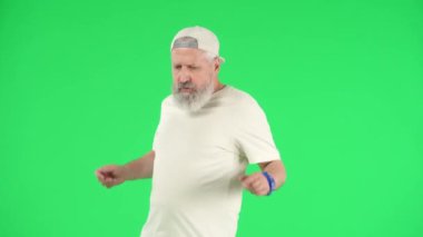 Yaratıcı yaşlılar ve modern yaşam tarzı konsepti. Chroma Key Green Screen 'de kıdemli hipster portresi, beyaz şapkalı havalı yaşlı adam ve müzik eşliğinde dans eden tişört. Reklam alanı, çalışma alanı modeli