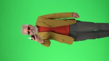 Yaratıcı yaşlılar konsepti. Şık ceketli, yeşil ekranda gözlüklü, kırmızı şarap içen kıdemli hippi portresi. Reklam alanı, çalışma alanı modeli. Dikey video.