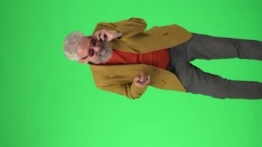 Yaratıcı yaşlılar konsepti. Şık ceketli, gözlüklü, yeşil ekranlı, akıllı telefondan konuşan, gülümseyen kıdemli hippi. Reklam alanı, çalışma alanı modeli. Dikey video.