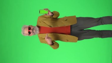 Yaratıcı yaşlılar konsepti. Akıllı telefon Chroma anahtar yeşil ekranlı gözlüklü son sınıf öğrencisinin portresi kameraya başparmaklarını doğrultuyor. - Reklam alanı, çalışma alanı modeli. Dikey video.