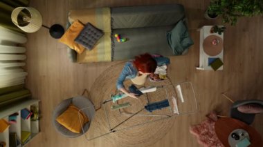 Üstteki karede bir çamaşır kurutma makinesi ve yanında da bir kanepe var. Sonra hamile bir kadın çamaşır sepetiyle odaya girer ve bebek kıyafetleri asar. Çamaşır yıkıyor. Üst görünüm.