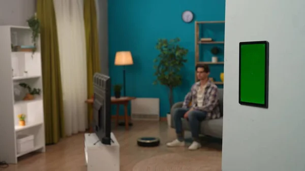 スマートハウスとモダンなライフスタイル広告コンセプト 近代的なアパートの閉鎖 壁にクロマキーグリーンスクリーン付きタブレット テレビを見ているソファの男 広告エリアワークスペースモックアップ — ストック写真