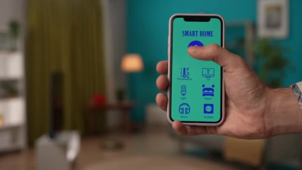 スマートハウスクリエイティブ広告コンセプト クローズアップショット男性の携帯電話 ランプ エアコン ロボットクリーナー スマートフォンアプリでカーテンを開き 画面インターフェイスのアイコンに焦点を当てる — ストック動画