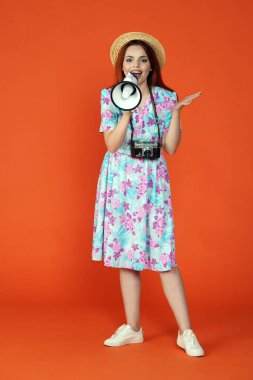 Seyahat ve tatil reklamları konsepti. Kadın modelin stüdyo fotoğrafı. Kameraya bakan bir kadın gülümsüyor, elinde megafon ve içinde bir şeyler reklamı var, turuncu arka planda izole edilmiş..
