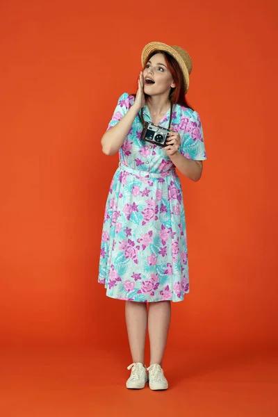 stock image Travelling and vacation advertisement concept. Studio shot of female model. Woman standing holding old film camera, looking surprised with open mouth holding hand up, isolated on orange background.