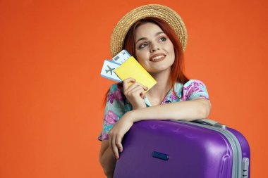 Seyahat reklam konsepti. Kadın modelin stüdyo fotoğrafı. Uçuş biletlerini tutan kadına yakın. Elleri bavulda, yukarı bakıyor, tatilin hayalini kuruyor, turuncu arka planda izole edilmiş..