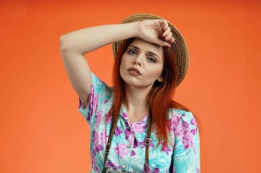 Seyahat reklam konsepti. Kadın modelin stüdyo fotoğrafı. Kameraya yorgun yüzlü, alnından el ele tutuşmuş, turuncu arka planda izole edilmiş bir şekilde bakan bir kadın..
