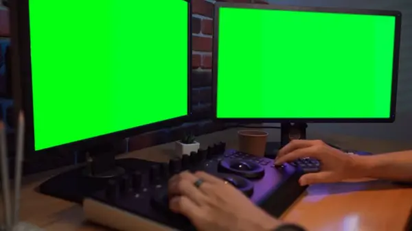 Video and photo editing creative concept. Freelancer working on agency from home. Closeup shot of man hands working at the desk using mixer editing video color settings, chroma key monitors.