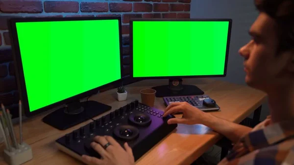 Video and photo editing creative concept. Freelancer working on agency from home. Closeup portrait of man working at the desk looking in chroma key monitors editing video settings using mixer.