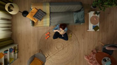 Yukarıdaki karede, hamile bir kadın bir odada koltuğun yanında oturuyor. Yanında halterler uzanıyor, elinde bir bardak tutuyor ve dinlenirken su içiyor. Vücut çalışıyor. Üst görünüm.