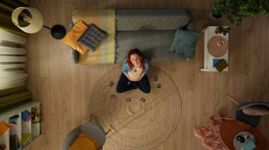 Tepeden çekimde, hamile bir kadın bir odada yerde oturuyor. Ultrason görüntülemesinin etrafında. Mutluluğu, neşeyi ifade eder, gülümser. Ailemize yeni birinin katılmasını bekliyoruz. Üst görünüm.