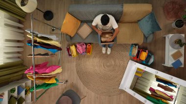 Alışveriş, eğlence ve yaşam tarzı reklam konsepti. Modern apartman oturma odasının en iyi manzarası. Kanepede oturan adam karton kutuyu açar ve aldığı pakete bakar, olumlu ifade..