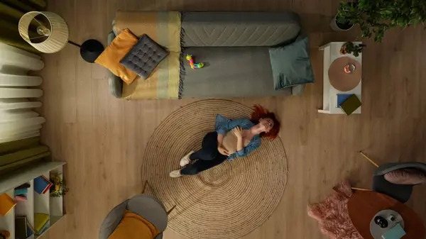 在上面的镜头中 房间里的一个孕妇躺在地板上 她控制着她的胃 她很痛苦 在痛苦中挣扎 旁边站着一张放着儿童玩具的沙发 顶部视图 — 图库照片