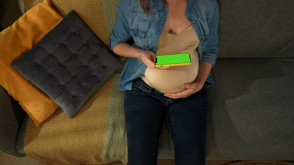 Primer Plano Muestra Una Mujer Embarazada Sentada Sofá Ella Sostiene —  Fotos de Stock