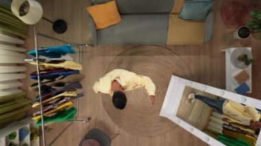 Alışveriş ve uygun yaratıcı reklam konsepti. Üst kat manzaralı bir oda. Adam akıllı telefondan selfie video blogu kaydediyor. Aynanın önünde birçok kıyafet deniyor. Hiçbir şeyi sevmiyor..