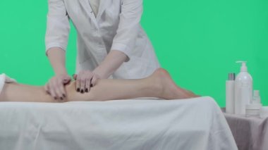 Vücut tonusu reklam konsepti. Güzellik kliniğini kapat, masaj masasında bir kadın, krom anahtar yeşil perde arka planı, terapist bacak masajı yapıyor. Reklam alanı, çalışma alanı modeli.
