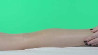 Vücut tonusu reklam konsepti. Güzellik kliniği odası, masaj masasında bir kadın, krom anahtar yeşil perde arka planı, masör yağ ile ayak masajı yapıyor, kapat. Reklam alanı, çalışma alanı modeli.