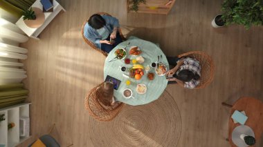 Aile bağı ve ilişki kavramı. Daire odasında bir sahne. Masada oturup kahvaltı yapan aile manzarası, baba, anne ve küçük kızı internetten aletlerle meşgul..