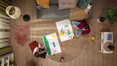 Yukarıdan çekilen resimde bir kadının ve çocuğun üzerine kendi çarşaflarını çiziyorlar. Yerde bir kanepe var, boyalar ve oyuncaklar. Eğleniyorlar, merak ediyorlar..