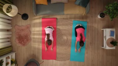 Yukarıdaki çekimde, bir kadın ve çocuk spor paspasının üzerinde bir odada duruyor. Yoga pozu verirken, kollarını öne doğru çekip geriliyorlar. Kadın kıza nasıl doğru yapılacağını öğretiyor..