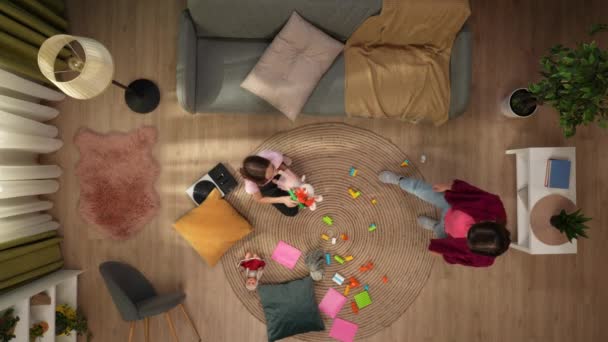 上のショットでは 女の子がおもちゃで遊んでいる部屋の床に座って 周りで混乱しています その後 母親はフレームに現れ 娘を叱責し おもちゃを遠ざけようとします — ストック動画