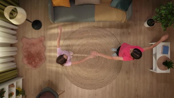 在上面的镜头中 一个女人和一个孩子 他们站在一个房间里 穿着运动服 彼此相对地进行体育锻炼 他们把胳膊伸到两边 伸着腿 顶部视图 — 图库视频影像